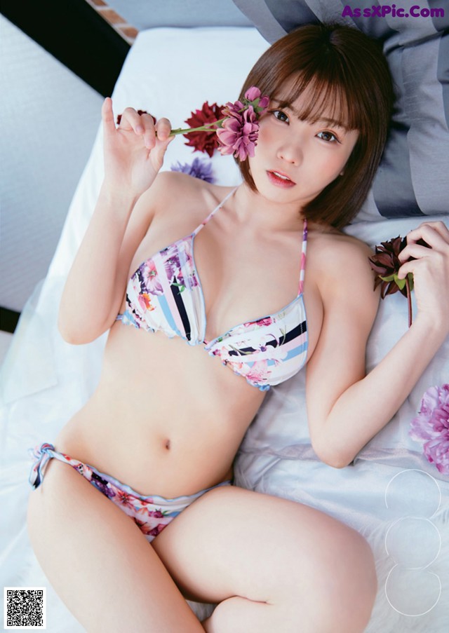 A woman in a bikini laying on a bed holding a flower.