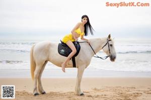 A woman in a yellow bikini standing next to a white horse.