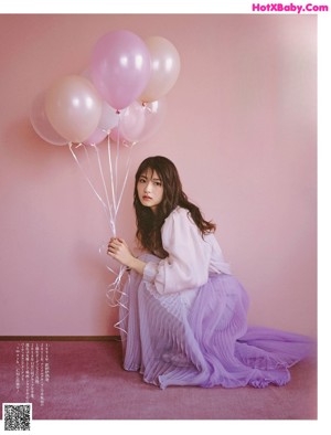 A woman sitting on a bench holding a bunch of balloons.