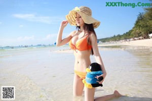 A woman in an orange bikini and a straw hat standing in the water.