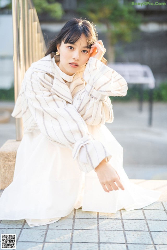 A woman in a white dress sitting on a bench.