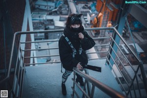 A woman in a black hoodie and cat ears is standing on some stairs.