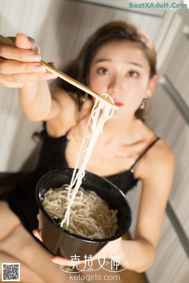 A woman holding chopsticks over a bowl of noodles.