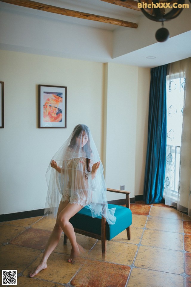 A woman in a white lingerie sitting on a blue chair.