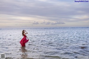 A woman in a red dress standing in the water.