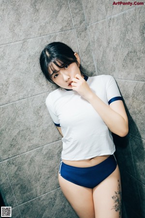 A woman in a white shirt and blue shorts standing in a bathroom.