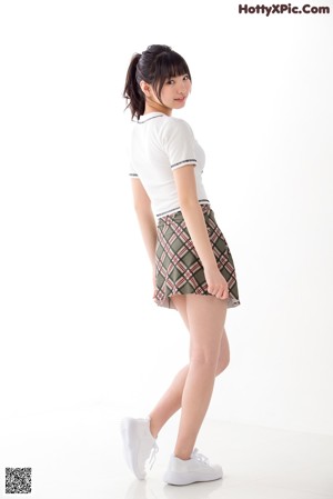 A woman leaning against a wall wearing a white shirt and a plaid skirt.