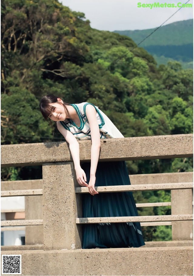 A woman leaning on a concrete railing with trees in the background.