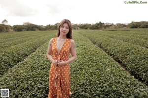 A woman in an orange polka dot dress standing in a field.