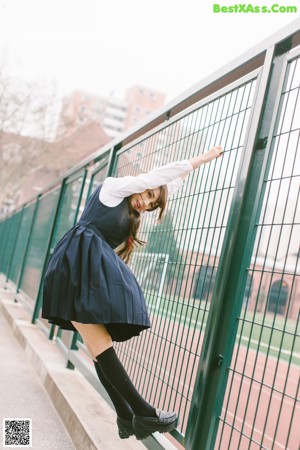 A young woman in a school uniform leaning against a window.