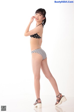 A woman in a black and white polka dot bikini leaning against a wall.