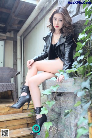 A woman in a black leather outfit sitting on a chair.